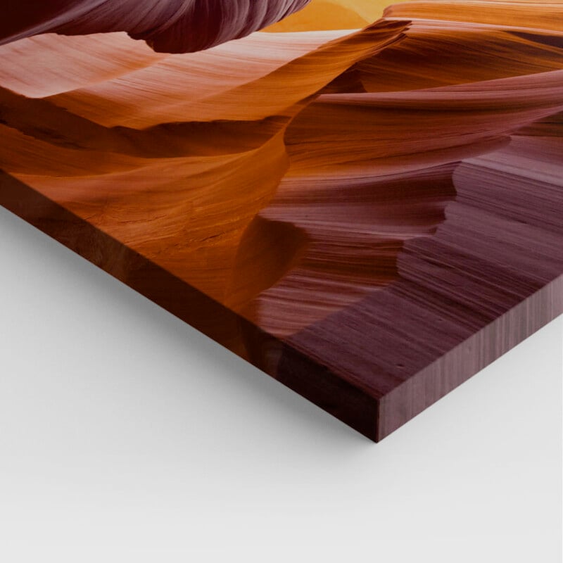 Close-up of a printed photo depicting the flowing, curved lines and rich red and orange hues of a canyon rock formation, mounted on a flat surface with clean edges, resembling a tabletop or panel.