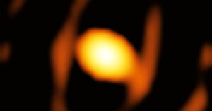 A blurred, glowing orange orb is surrounded by darker, abstract shapes on a black background, resembling a celestial object or distant light source.