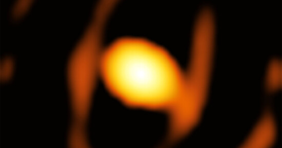 A blurred, glowing orange orb is surrounded by darker, abstract shapes on a black background, resembling a celestial object or distant light source.