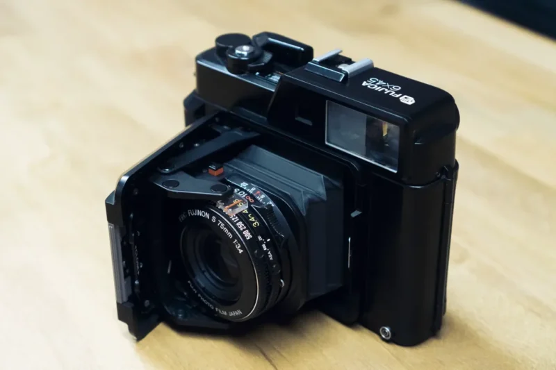 A vintage Fujifilm medium format camera with a fold-out lens is placed on a wooden surface.