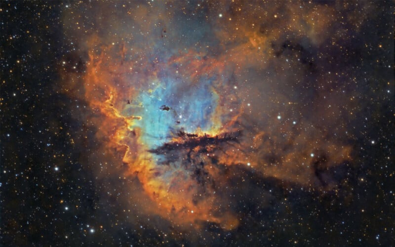 A vivid image of the Wizard Nebula showcasing bright orange, blue, and black swirling clouds of gas and dust. Countless stars are scattered throughout, set against the deep blackness of space.