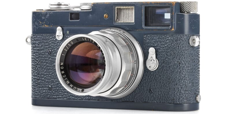 A vintage rangefinder camera with a worn black leather body and a silver lens. The camera features various knobs and buttons, and the lens is engraved with "SUMMICRON 1:2/50". The body shows signs of age and use.