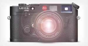 A Leica M6 camera with a classic black design is shown from the front. The camera has textured grips, a lens attached, and a red Leica logo above the lens, with a bright glare effect over the lens.