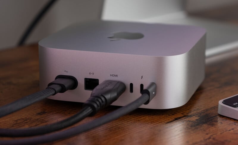 A silver computer device with multiple ports on the back, including HDMI and USB-C, is connected to several black cables. It is placed on a wooden surface.