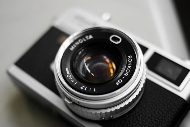 Close-up of a vintage Minolta camera featuring a Rokkor-QF 1:1.7 40mm lens. The camera is positioned at an angle, showcasing the lens details with a blurred background.