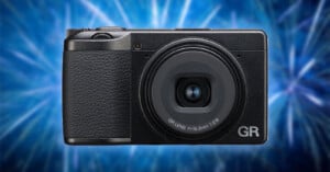 A compact black digital camera with a textured grip is centered against a vibrant blue, abstract background. The lens is labeled "GR LENS f=18.3mm 1:2.8" on the front.