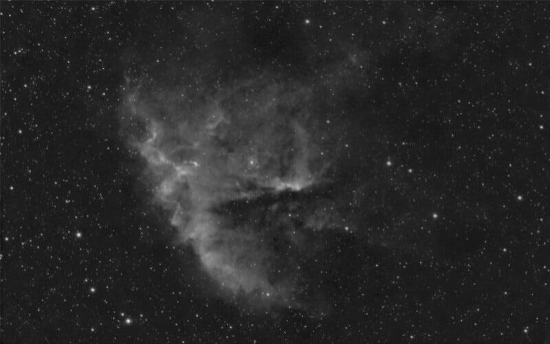 A grayscale image of a nebula in deep space. The nebula has wispy structures and varying textures, surrounded by numerous stars scattered across the dark background.