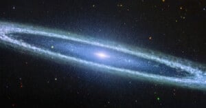 A cosmic image of a spiral galaxy with a bright core and blue, wispy arms extending outward. Stars of varying sizes and colors are scattered across the dark, expansive background of space.