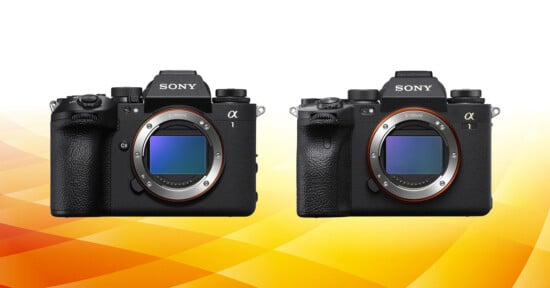 Two Sony Alpha mirrorless cameras side by side on a yellow-orange gradient background. The cameras have prominent lenses with silver edges and dials on top.