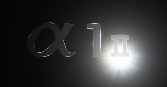 A chrome representation of the Greek letter "Alpha," the number "1," and the Roman numeral "II" is illuminated against a dark background with a bright light source on the right.