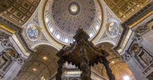 The ornate interior of St. Peter's Basilica in Vatican City, showing a detailed view of the dome and the bronze Baldachin by Bernini. Intricate designs and religious art decorate the majestic architecture.