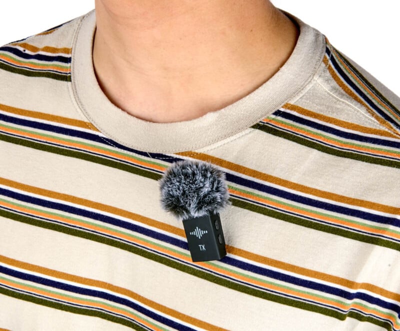 A person wearing a striped shirt with a small clip-on microphone attached, featuring a furry windscreen.