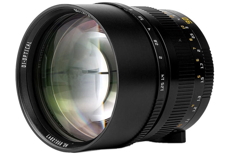 A camera lens with a wide, reflective front element. The focusing ring shows various focal length markings. The lens body is sleek and black, featuring yellow and white text indicating aperture and focal length.