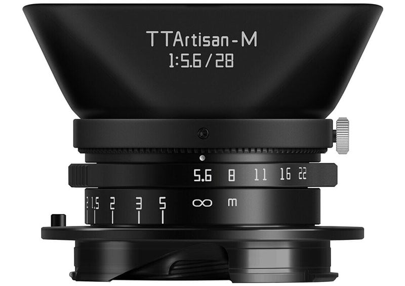 Close-up of a TTArtisan-M 28mm f/5.6 camera lens, showing the aperture and focus rings with engraved markings. The lens features a compact design with a smooth black finish and a wide lens hood.