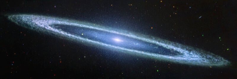 A spiral galaxy with a bright core and wide, flat arms filled with stars and cosmic dust, set against a dark background dotted with smaller, distant stars.