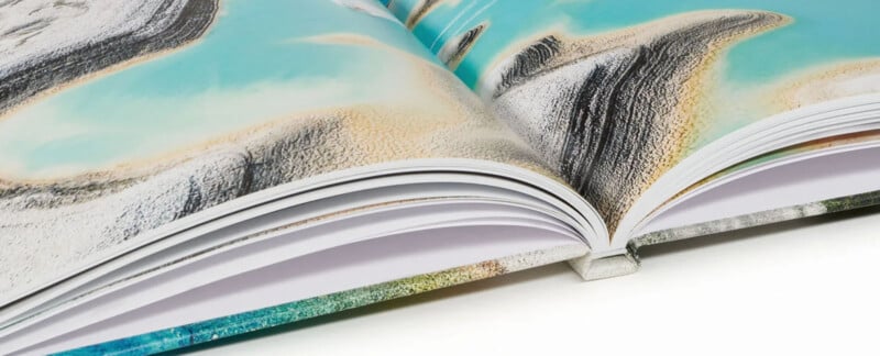 A close-up of an open book showing colorful artwork across its pages. The image highlights the spine and the vibrant, textured detail of the illustrations on the glossy paper.