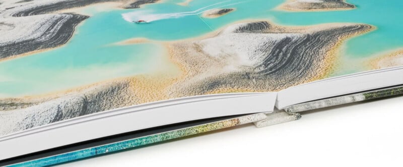 An open book displaying a vibrant aerial photograph of a turquoise coastline with sandy and rocky formations. A small boat is visible in the water, creating a contrast with the natural scenery. The book's pages are slightly curved.