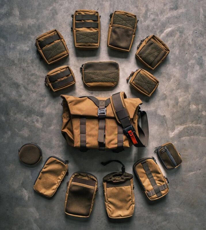 A brown messenger bag is surrounded by various matching pouches of different shapes and sizes, arranged in a circular pattern on a concrete floor. The bag has a shoulder strap and buckle, while the pouches have mesh and strap details.