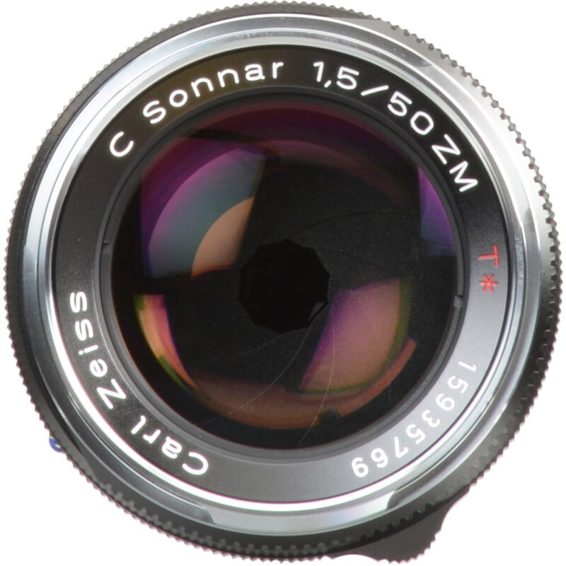 Close-up view of a Carl Zeiss C Sonnar 1.5/50 ZM camera lens. The lens features a prominent aperture opening and engraved details, with reflections visible on the glass surface.