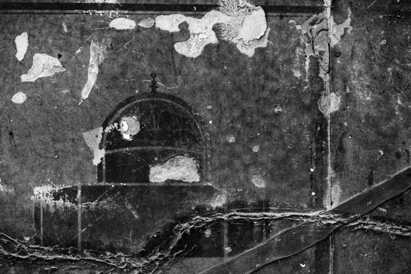 A weathered wall with peeling⁣ paint and visible cracks.⁣ The ‌surface features what ⁣appears to be a faded silhouette of a dome⁢ structure. The black-and-white texture emphasizes the aged and​ distressed​ condition.