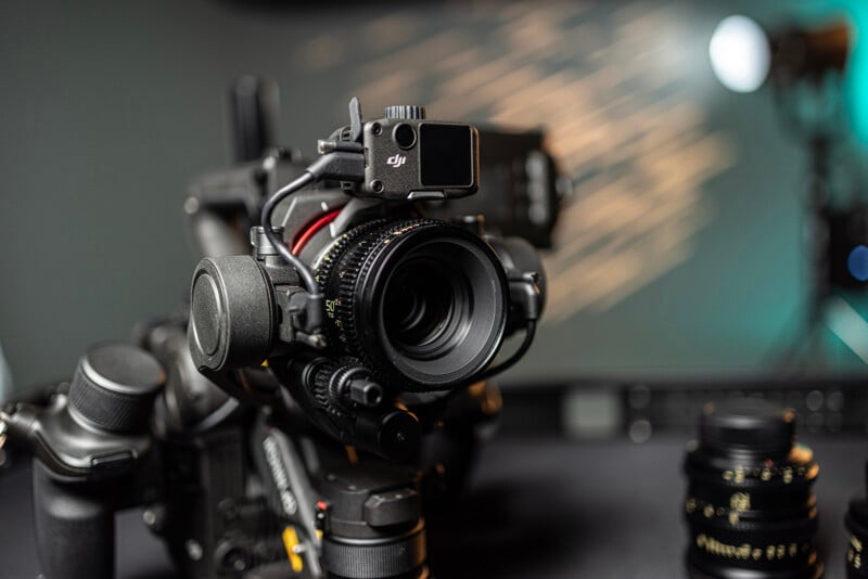 Close-up of a professional camera mounted on a gimbal, surrounded by various camera gear. The setup is in a studio with blurred lighting in the background, creating a cinematic effect.