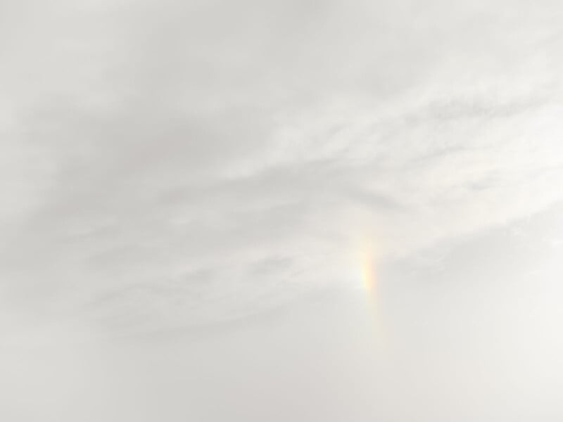 A faint rainbow appears in a cloudy, pale sky. The soft, diffused light creates a serene, monochromatic atmosphere with subtle variations in gray and white hues.