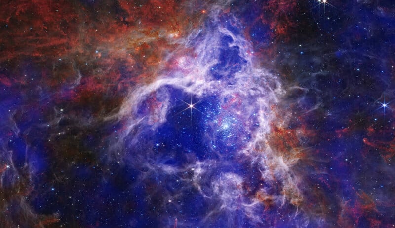 A vivid image of a nebula in space, showcasing swirling clouds of red, blue, and purple gases. Bright stars are scattered throughout, set against a dark background, creating a stunning cosmic scene.