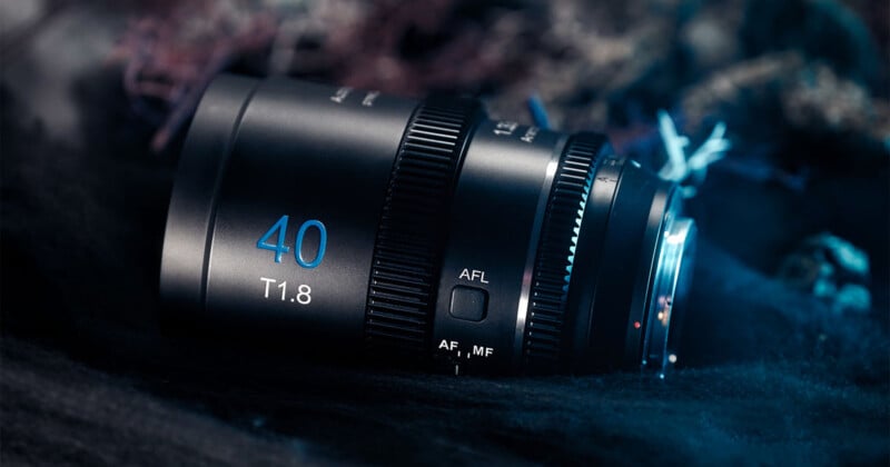 A close-up of a camera lens on a dark, textured surface. The lens is black with a blue "40 T1.8" marking. Various controls and switches are visible, including an AFL button and an AF/MF switch. The lighting is dim and slightly bluish.