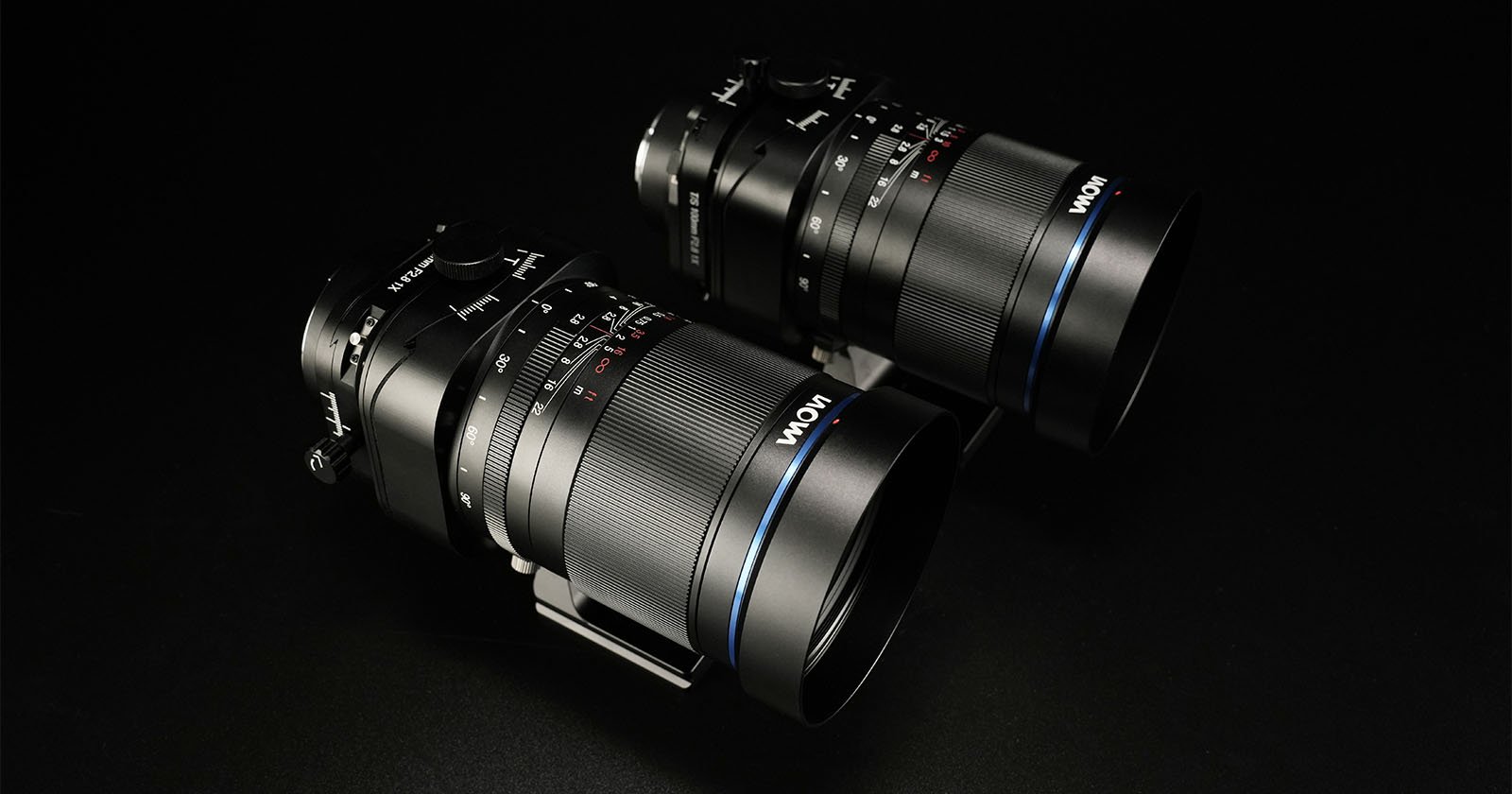 Two Laowa camera lenses are displayed against a black background. The lenses are positioned side by side, showcasing their sleek design and intricate focus rings, with visible brand markings in blue accents.