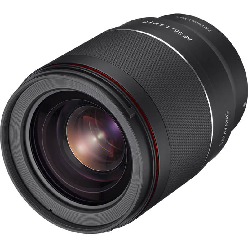 Close-up of a black camera lens with a textured grip, featuring red accents near the front. The lens is positioned diagonally against a white background, showcasing its glass elements and markings.