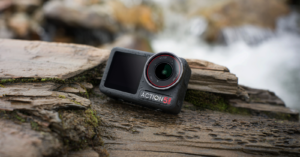 A rugged action camera with "ACTION 5S" branding is placed on wet, textured wooden surfaces near a flowing stream. The scene conveys a sense of adventure and durability in outdoor settings.