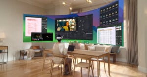 A person wearing a VR headset sits at a table in a modern living room. They're engaging with a virtual display featuring video editing software, spreadsheets, and planning documents projected in front of them. The room has wooden floors and large windows.