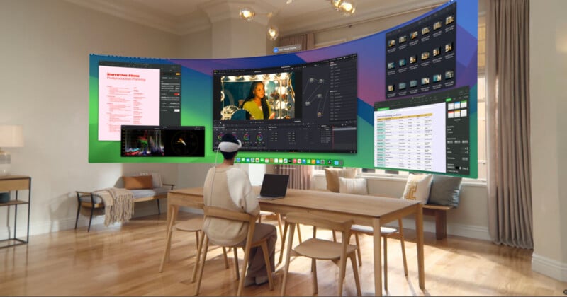 A person wearing a VR headset sits at a table in a modern living room. They're engaging with a virtual display featuring video editing software, spreadsheets, and planning documents projected in front of them. The room has wooden floors and large windows.