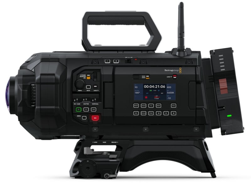 A professional digital video camera with a large lens, control buttons, and a mounted display screen showing recording time. It has a handle on top, adjustment dials, and an antenna on the side. The camera is predominantly black.