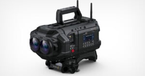 A professional black video camera with dual lenses and a handle on top. Numerous buttons and a small display screen are visible on the side. The camera is designed for advanced filmmaking.