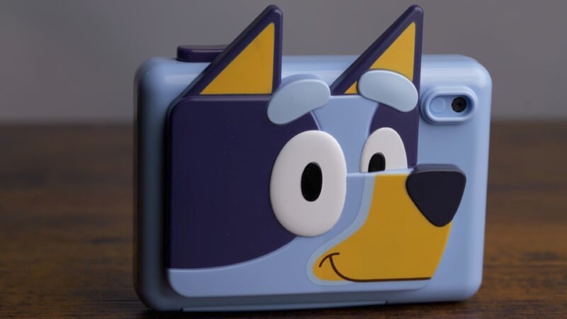 A blue smartphone case decorated with a cartoon character resembling a dog, featuring large eyes, pointy ears, and a smiling face. The design is bold and colorful, adding a playful touch to the phone.