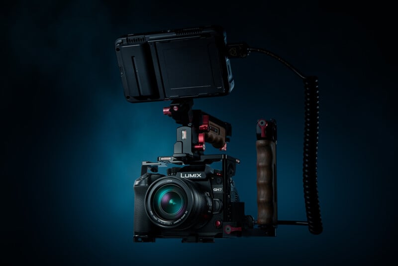 A Lumix GH7 camera with an accessory rig, including a top monitor and a wooden side handle, is set against a dark blue background.