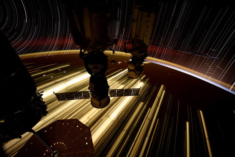 A long-exposure photo of a spacecraft in orbit, with streaks of light trails from stars in the background. The curvature of Earth is visible on the horizon, with a glowing band of light from the atmosphere.