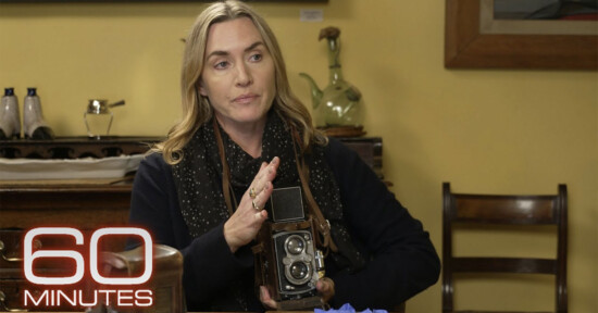 A woman with long blonde hair sits indoors, holding a vintage camera. She is surrounded by various objects and appears to be speaking. The "60 Minutes" logo is visible in the bottom left corner.