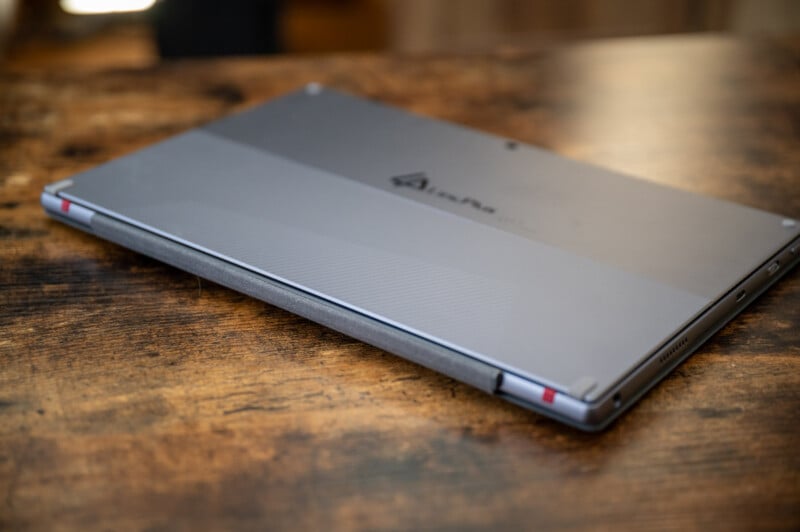 A closed laptop with a sleek, metallic design rests on a wooden surface. The laptop is positioned with its hinge facing outward, showing a subtle logo on the top.