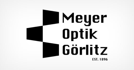 Logo of Meyer Optik Görlitz featuring three black geometric shapes aligned vertically, resembling a stylized "M" on the left. The text "Meyer Optik Görlitz" is on the right, with "EST. 1896" below. Black on a white background.