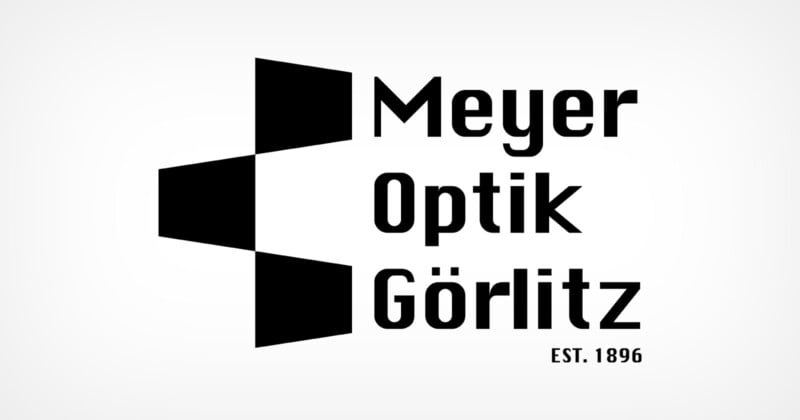 Logo of Meyer Optik Görlitz featuring three black geometric shapes aligned vertically, resembling a stylized "M" on the left. The text "Meyer Optik Görlitz" is on the right, with "EST. 1896" below. Black on a white background.