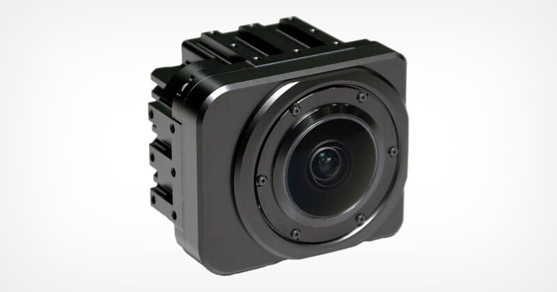 A square, compact black camera with a sleek design, featuring a circular lens in the center. It has a matte finish with subtle detailing, set against a plain white background.