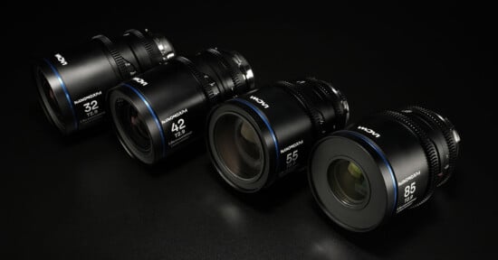 A row of four black Laowa camera lenses with different focal lengths (32mm, 42mm, 55mm, 85mm) on a dark surface. Each lens features a blue accent ring and white text indicating the specifications.