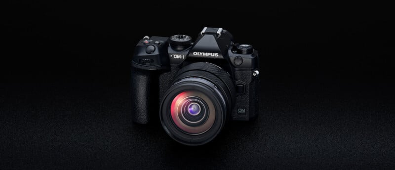 A black Olympus digital camera with a large lens is centered against a dark background. The lens reflects a subtle red light, highlighting its curves and details.