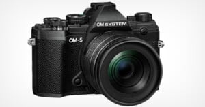 A black OM System OM-5 camera with a large lens, featuring various dials and buttons on the top and side, set against a plain white background.