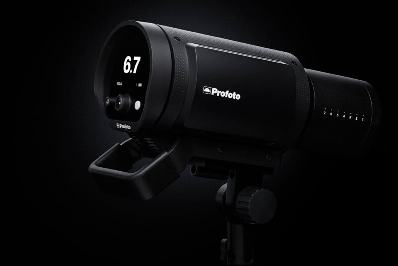 A sleek black Profoto studio light with a digital display showing "6.7" and various control buttons. It is mounted on a stand against a dark background.