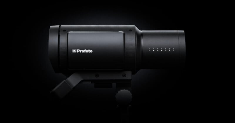 A black studio light against a dark background. The word "Profoto" is printed on the side, and there are adjustment numbers visible. The design is sleek and cylindrical, with a handle underneath.