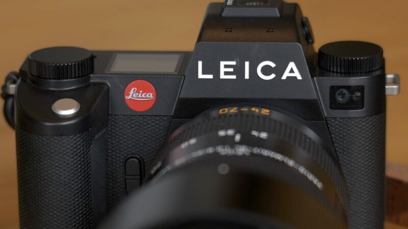 Close-up view of a black Leica camera with its logo prominently displayed on the top. The camera's lens is partially visible in the foreground.