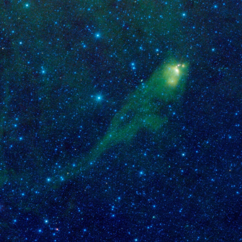 A colorful cosmic scene featuring a green, fish-shaped nebula against a backdrop of blue and white stars in space. The nebula appears luminous and prominent, surrounded by a dense field of twinkling stars.